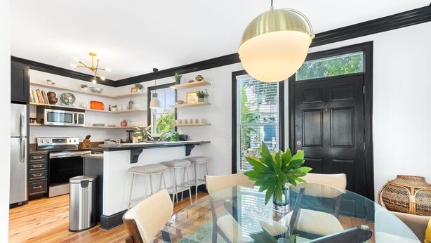 A modern kitchen with a dining area, featuring a glass table, white chairs, and a hanging light fixture.