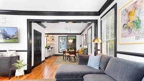A modern living room with a grey sofa, wooden flooring, and a dining area with a table and chairs.