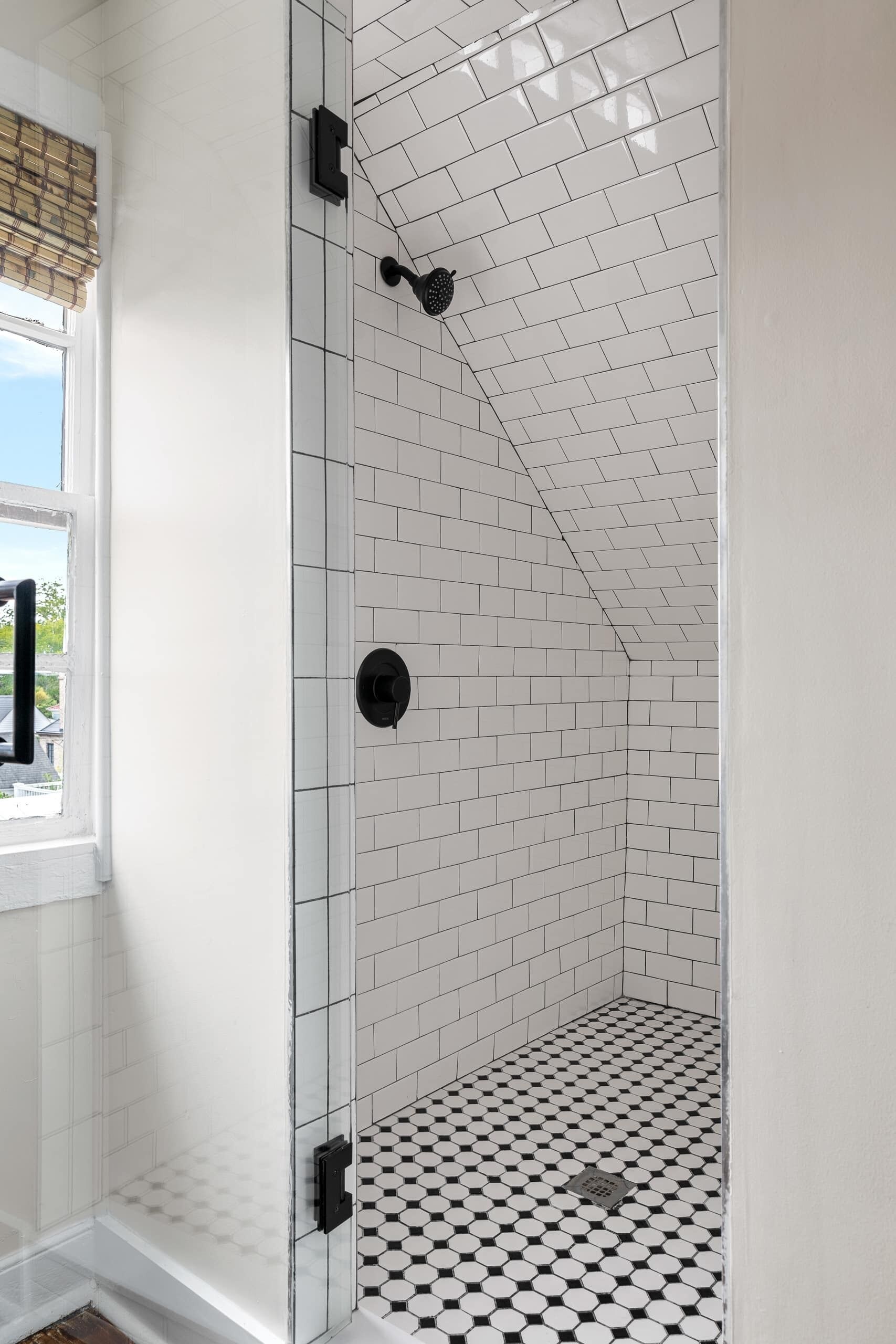 A shower with white tiled walls and a black and white checkered floor.