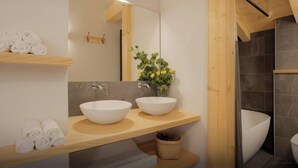 Une salle de bain moderne avec deux vasques blanches, un meuble-lavabo en bois, un miroir, un porte-serviettes et un vase avec des fleurs.