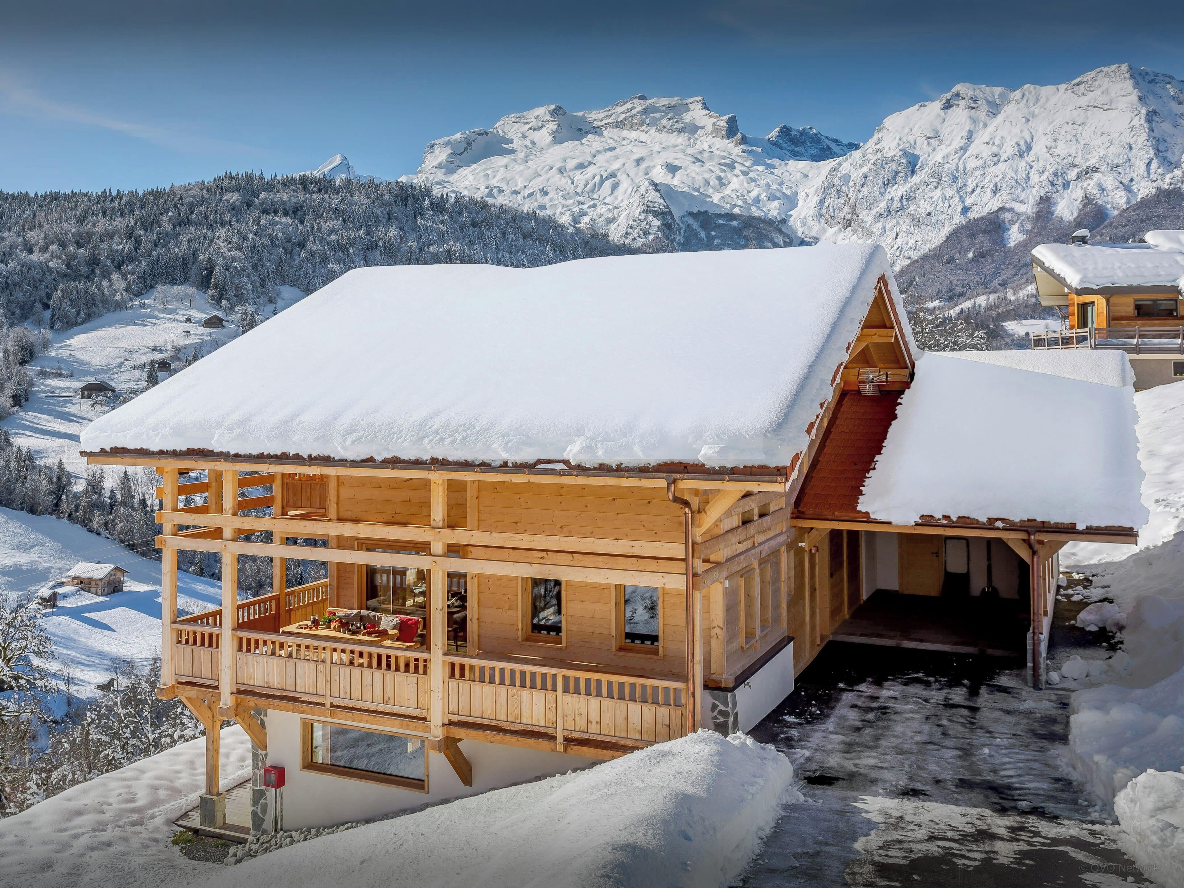 Una baita di legno con un balcone, con alle spalle un paesaggio montano innevato.