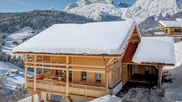 Una baita di legno con un balcone, con alle spalle un paesaggio montano innevato.