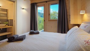 Une chambre avec un grand lit, une fenêtre avec des rideaux, une table de chevet avec une lampe, et une vue sur l’extérieur.