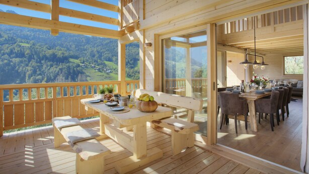 Une terrasse en bois avec une table dressée pour le petit-déjeuner, donnant sur une vallée boisée.