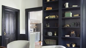 Un salon moderne avec deux fauteuils gris, un pouf en cuir, une bibliothèque sombre et un luminaire suspendu au plafond.