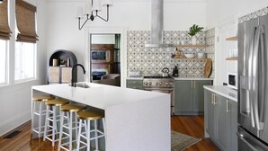 A modern kitchen with a central island, bar stools, a stove, and a refrigerator. - The Monroe | Award-Winning Renovated Historic Home (Charleston)