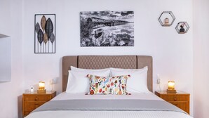 A neatly made bed with a patterned pillow, two bedside tables with lamps, and wall art including a leaf pattern and a black and white landscape. - Mikros Paradisos Pelion (Άγιος Βλάσιος)