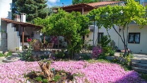A garden with pink flowers, a wooden bench, and a building with a tiled roof. - Mikros Paradisos Pelion (Άγιος Βλάσιος)