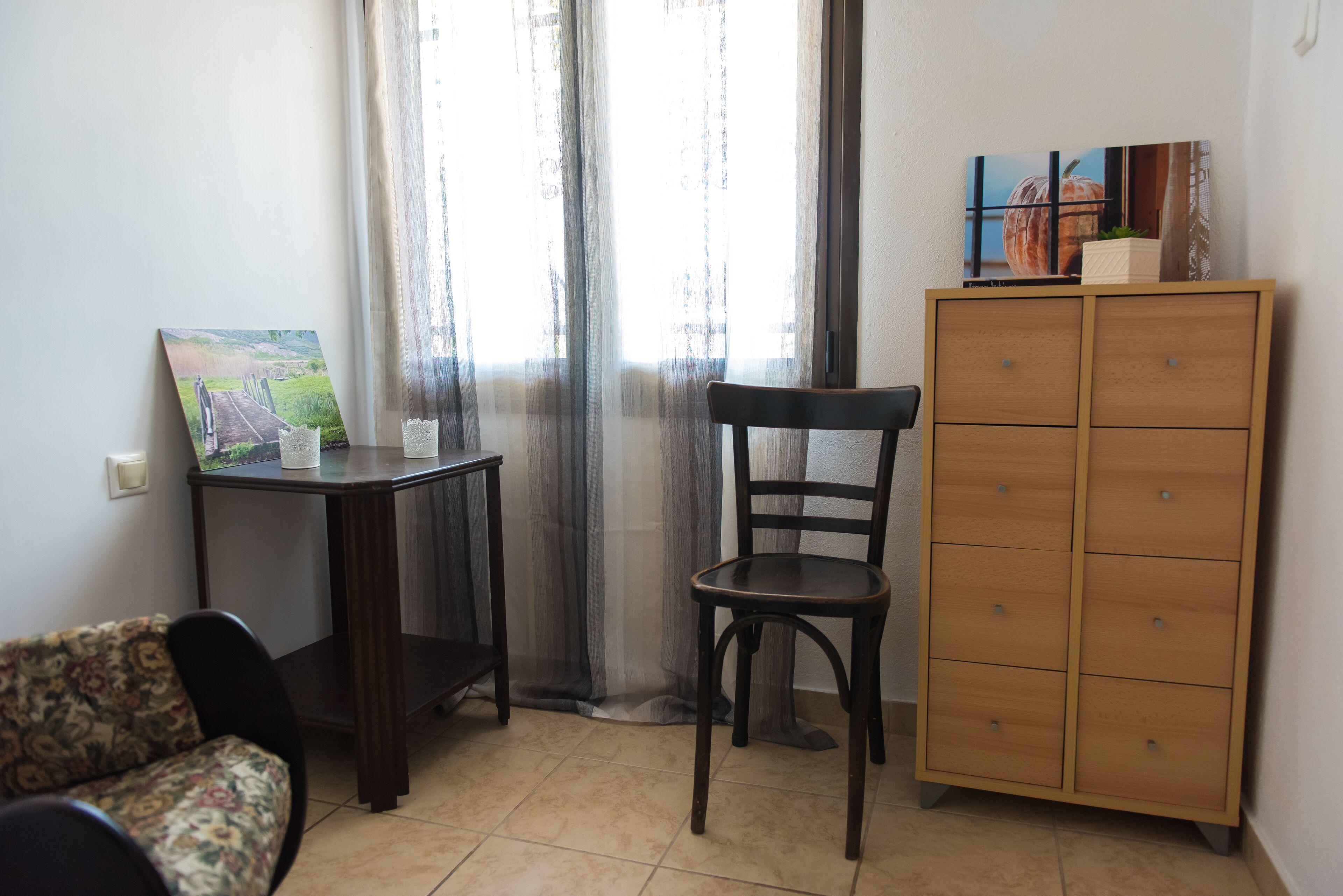 Una stanza con un armadio in legno, una sedia, un tavolino con un quadro e un divano.