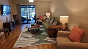 Una sala de estar con televisor, sofá, mesa de centro y vistas a través de un ventanal.