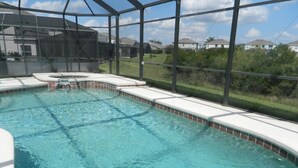 A clear swimming pool with a glass enclosure, surrounded by a white deck and a view of a residential area.