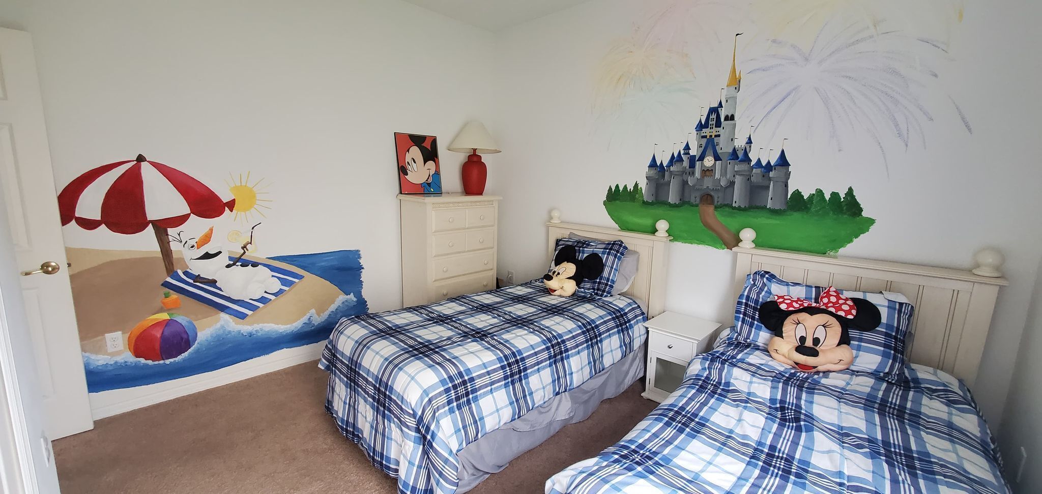 A child's bedroom with two beds, each with a Mickey Mouse pillow, a beach mural, and a castle mural on the wall.