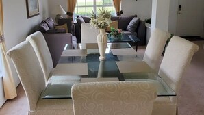 A living room with a glass coffee table, white patterned chairs, a sofa, and a vase with flowers.