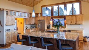 A spacious kitchen with wooden cabinets, a large island with bar stools, and a view of the outdoors through large windows.