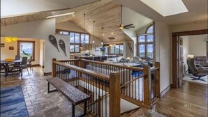 A spacious open-plan living area with a wooden ceiling, large windows, and a view of the outdoors.