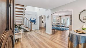 A spacious living area with a wooden staircase, a dining area with a blue rug, and a kitchen visible through an archway. - Big East Beach Home with Pool (Saint Simons Island)