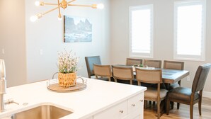 A modern kitchen with a central island, dining table, and chairs. There is a chandelier above the island and a painting on the wall. - Adventure Awaits in Southern Utah | Pool + Resort Style Amenities | Come Adventure with Family! (Washington)