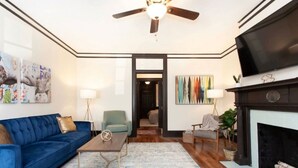 A living room with a blue sofa, a wooden coffee table, a fireplace, and a television. - Modern Midtown Retreat (Montgomery)