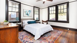 A bedroom with a bed, a desk, a chair, a ceiling fan, and large windows with blinds. - Modern Midtown Retreat (Montgomery)