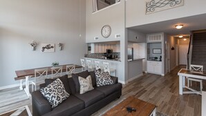 A modern living room with a sofa, coffee table, and a dining area with chairs and a table. A kitchen is visible in the background with white cabinets and a clock on the wall. - Beautiful Remodeled Luxury Waterfront Property- 3BR/2.5 bath-Sleeps 11!!! (Montgomery)