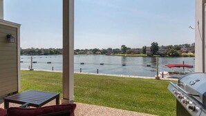 A covered patio with a view of a lake, a grill, and a red umbrella.