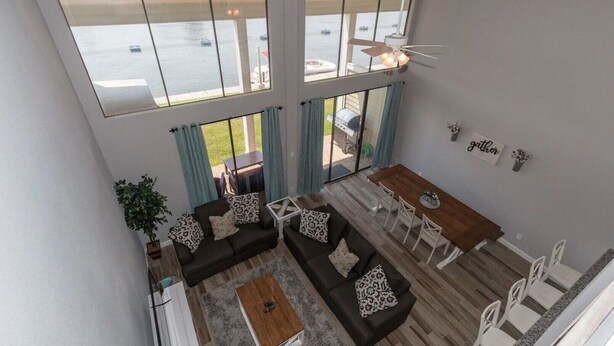 A spacious living area with a large window overlooking a body of water, a dining area with a table and chairs, and a ceiling fan.