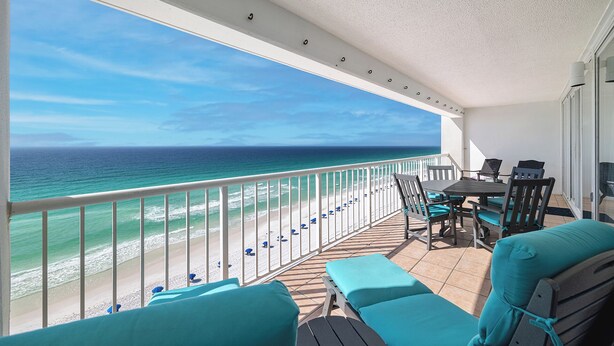 Een balkon met uitzicht op de oceaan, een tafel met stoelen en een zithoek met kussens.