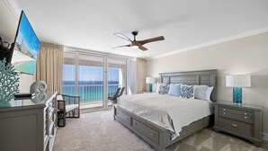 Een slaapkamer met een groot bed, een plafondventilator, een televisie en een balkon met uitzicht op de oceaan.