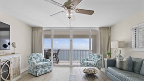 A spacious living room with a ceiling fan, a large sliding glass door leading to a balcony, a sofa, two armchairs, and a coffee table. - Seas the day - Destin Gulfgate 1006! (Destin)