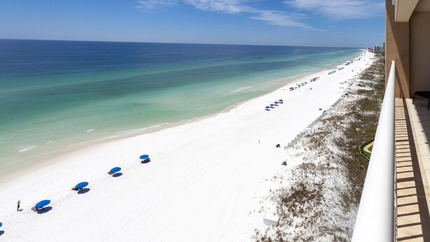 A beach view from a balcony with a clear sky, a sandy beach, and a row of blue umbrellas. - Seas the day - Destin Gulfgate 1006! (Destin)