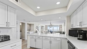 A modern kitchen with white cabinetry, a central island, and a built-in dishwasher. - Seas the day - Destin Gulfgate 1006! (Destin)