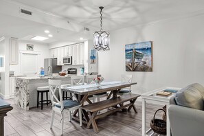 Een moderne keuken met witte kasten, een centraal eiland en een eethoek met een glazen tafel en houten banken.