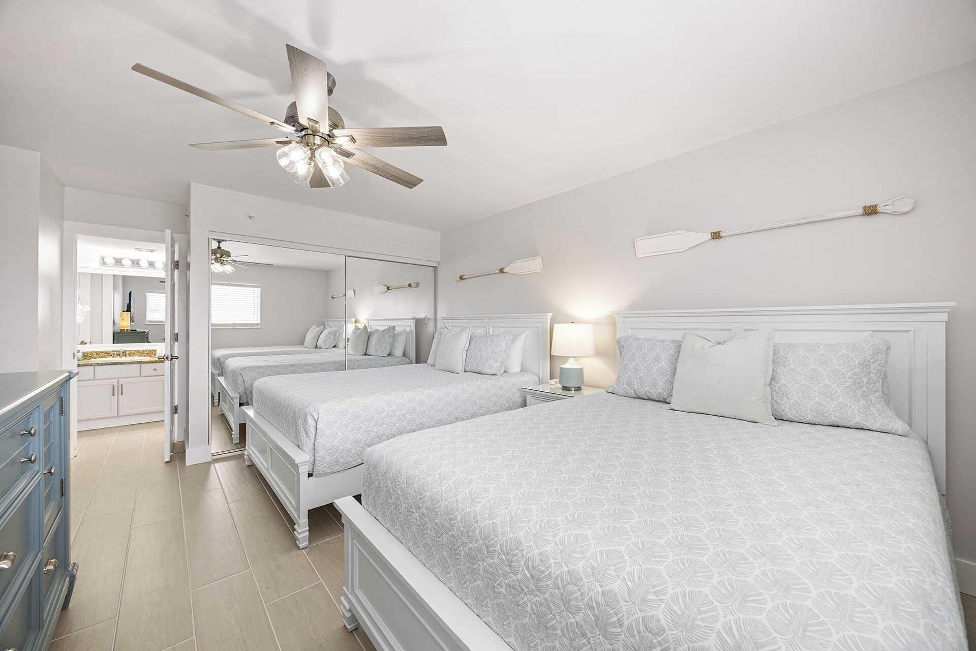 A bedroom with two beds, a ceiling fan, and a bathroom with a mirror and sink.