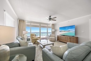 A spacious living room with a balcony, a ceiling fan, a large flat-screen TV, and a view of the beach. - Shore Beats Work - Destin Gulfgate 0201! (Destin)