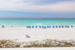 A beach with white sand, a row of blue umbrellas, and a clear blue ocean. - Shore Beats Work - Destin Gulfgate 0201! (Destin)