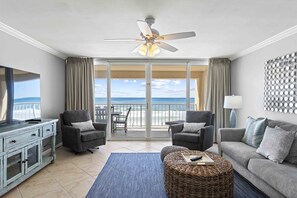 A living room with a balcony, grey sofas, a TV, and a ceiling fan.