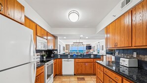 Une cuisine moderne avec des meubles en bois, un plan de travail noir et une vue sur l’océan grâce à de grandes fenêtres.