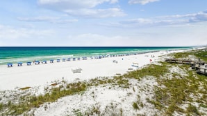 Une plage de sable blanc, des parasols bleus et un ciel dégagé.