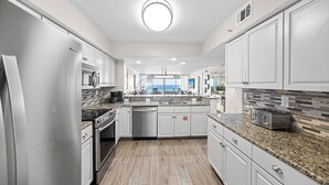 A modern kitchen with white cabinetry, granite countertops, a built-in oven, and a view to the outside. - Wait 'n Sea - Destin Gulfgate 0205! (Destin)