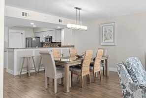 Un comedor con mesa de madera y sillas de mimbre, una cocina al fondo y una lámpara en el techo.