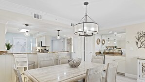 A spacious dining area with a large table, white chairs, and a decorative bowl centerpiece. - Destin Gulfgate 0206, Beachfront Condo in Heart of Destin! (Destin)