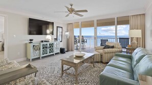 A spacious living room with a large window offering a view of the ocean, a ceiling fan, a flat-screen TV, and a patterned rug. - Destin Gulfgate 0206, Beachfront Condo in Heart of Destin! (Destin)