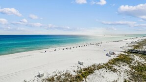 Uma extensa praia de areia com águas azul-claras e algumas pessoas.