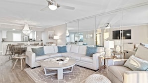 A spacious living room with a white sectional sofa, a round coffee table, and a dining area with wooden chairs. - Feeling tip'Sea - Destin Gulfgate 0403! (Destin)