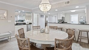 A modern kitchen with white cabinets, a central island, and a dining area with a round table and wicker chairs. - Feeling tip'Sea - Destin Gulfgate 0403! (Destin)
