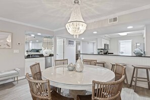 A modern kitchen with white cabinets, a central island, and a dining area with a round table and wicker chairs. - Feeling tip'Sea - Destin Gulfgate 0403! (Destin)