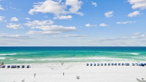 Ein Strand mit weißem Sand und einem klaren, blauen Meer unter einem teils bewölkten Himmel.