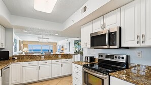 Eine moderne Küche mit weißen Schränken, Granitwerkplatten, Edelstahlgeräten und Meerblick durch große Fenster.