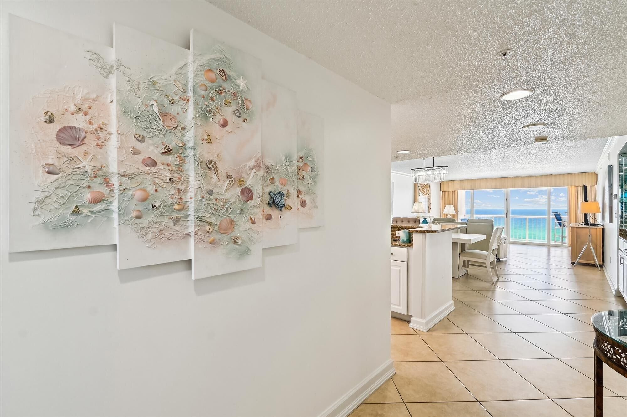 A spacious room with a large window offering a view of the ocean, a dining area with a view, and a modern kitchen.