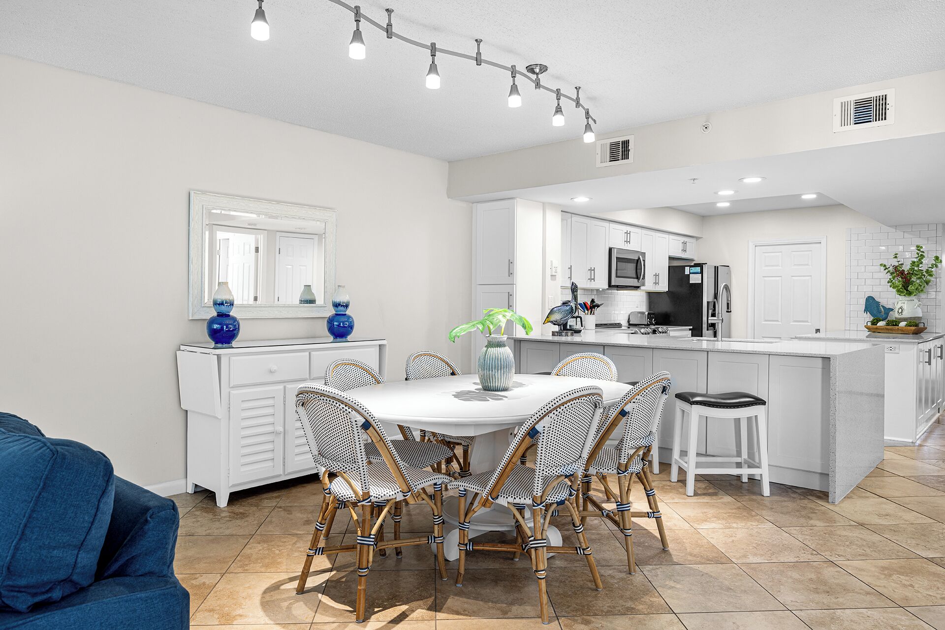 A modern kitchen with white cabinetry, a central island, and a dining area with wicker chairs.